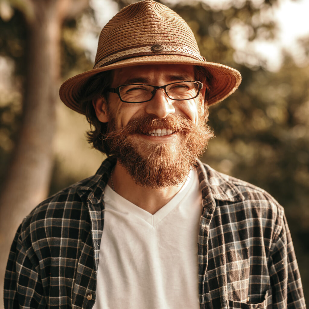 Smiling bearded man in glasses and hat in nature