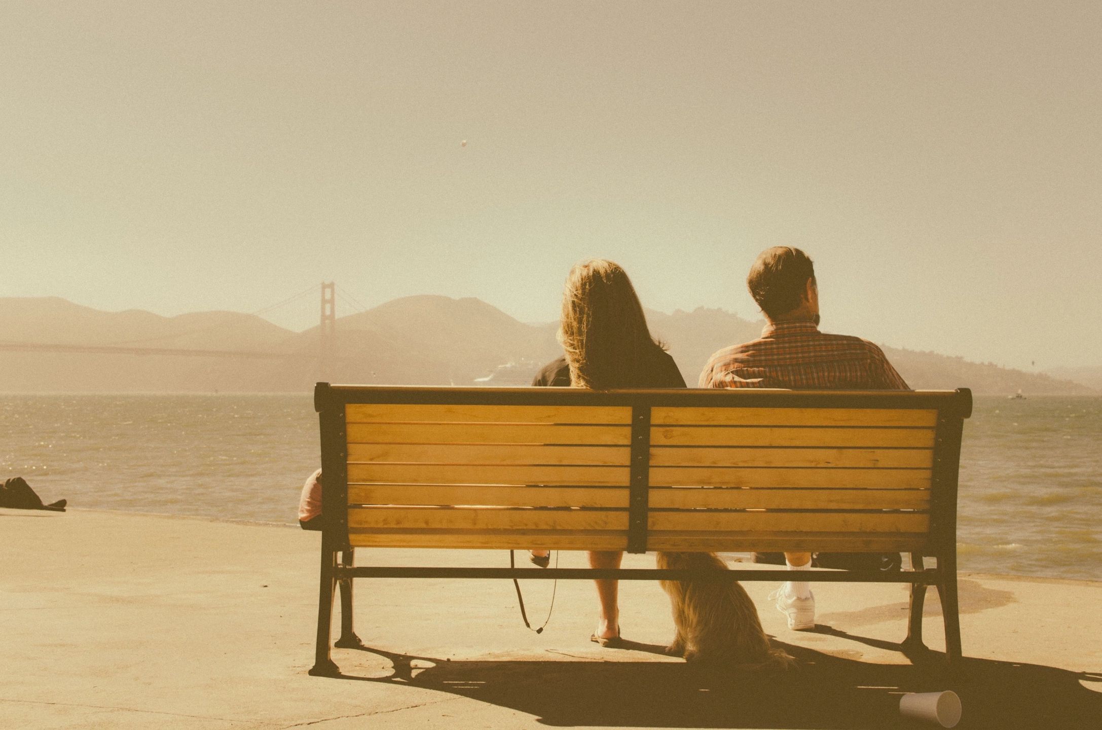 two people sitting on a bench in a hazy, yet bright open location