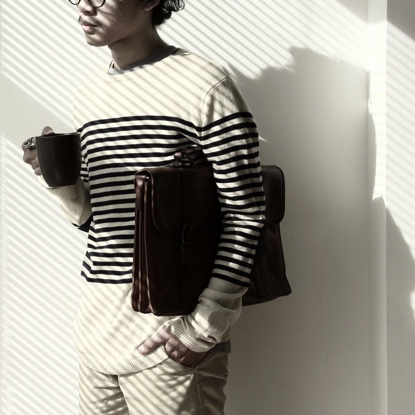 person leaning against a wall holding a mug and a brief case